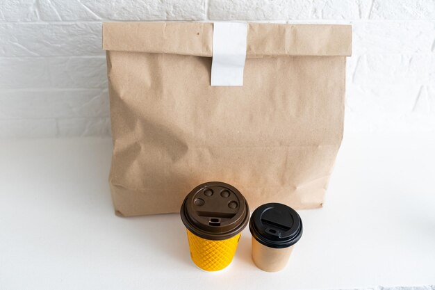 Fast food packaging set. Paper coffee cups in holder, food box, brown paper bag on the table.