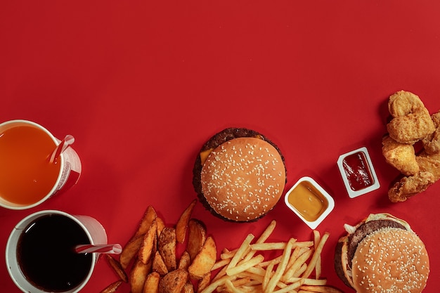 Fast food schotel bovenaanzicht vlees hamburger chips en glas drank op rode achtergrond afhaalmaaltijden...