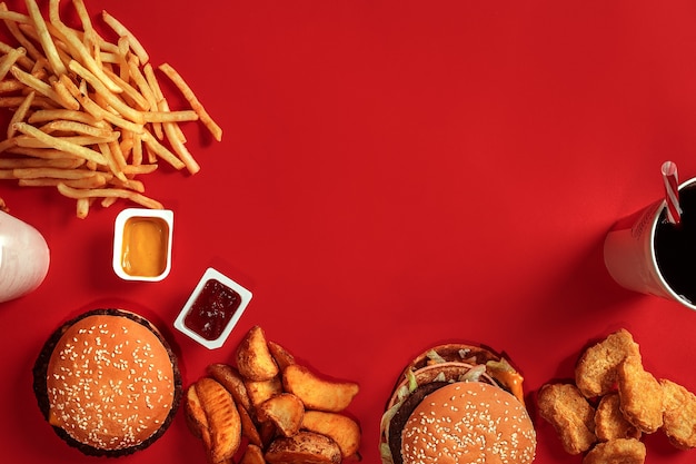 Fast food schotel bovenaanzicht vlees hamburger chips en glas drank op rode achtergrond afhaalmaaltijden...