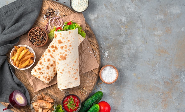 Fast food: shawarma, burrito on a gray wall with ingredients. Top view, copy space.