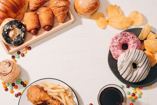 Fast food e concetto di cibo malsano - primo piano di snack fast food e bevanda a base di cola sul tavolo bianco