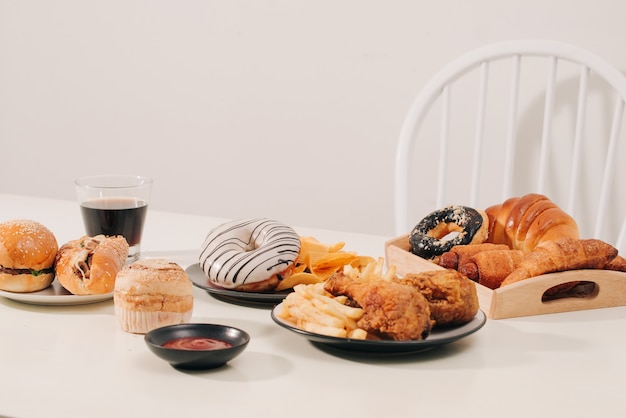 패스트푸드와 건강에 해로운 식사 개념 - 햄버거나 치즈버거, 튀긴 오징어 링, 감자튀김, 음료, 케첩을 나무 탁자에 올려 놓습니다.
