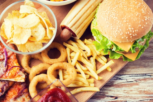 Photo fast food and unhealthy eating concept - close up of hamburger or cheeseburger, deep-fried squid rings, french fries hotdog and potato chips on wooden table top view