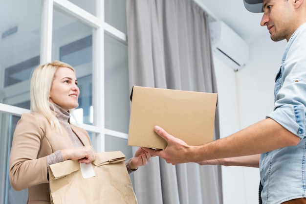 Fast and reliable service. Cheerful young delivery man giving a cardboard box to young woman while standing at the entrance of her apartment