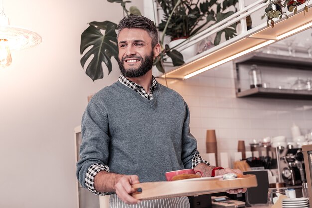 Fast service. Joyful pleasant man smiling while bringing order to the table