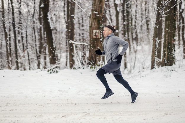 雪の降る冬の日に自然の中で全力疾走する速いスポーツマン。冬のフィットネス、有酸素運動、寒さ