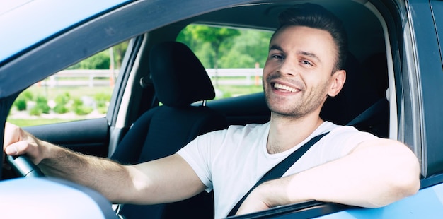 Пристегните ремни безопасности в своем автомобиле. Счастливый красивый молодой человек за рулем своей машины и улыбается. Возбужденный водитель в городском городе. Электро автомобиль, автомобиль будущего
