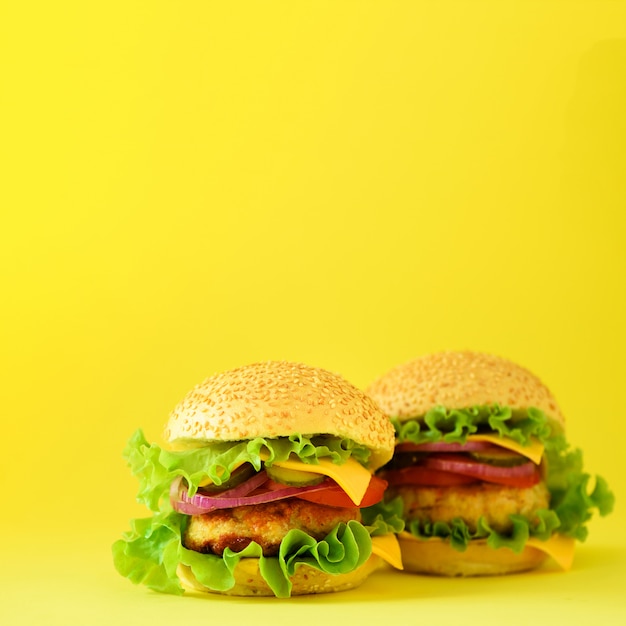 Fastfood concept. Vierkant gewas. Sappige zelfgemaakte hamburgers op gele achtergrond. Afhaalmaaltijd. Ongezond dieetkader