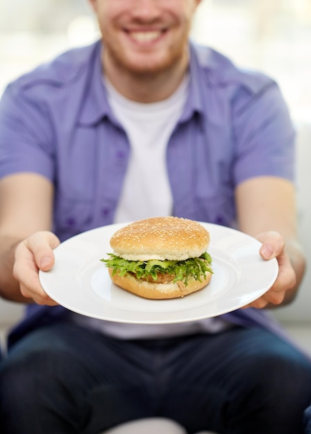 fastfood, ongezond eten, mensen en junkfood - close-up van gelukkige man met hamburger op bord thuis