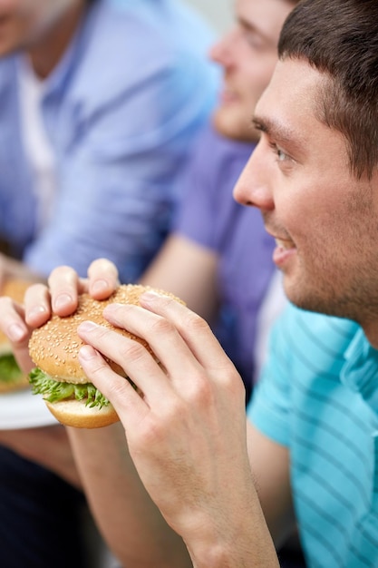 fastfood, ongezond eten, mensen en junkfood - close-up van gelukkige vrienden die thuis hamburgers eten