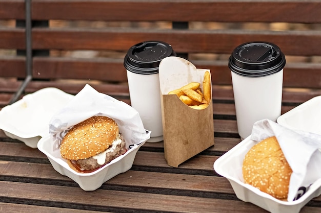 Foto fastfood papieren bekers met koffie hamburger dozen en frietjes op een park bankje takeaway voedsel concept