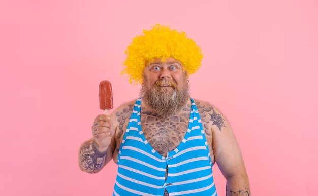 Толстый изумленный мужчина с бородой и париком ест эскимо