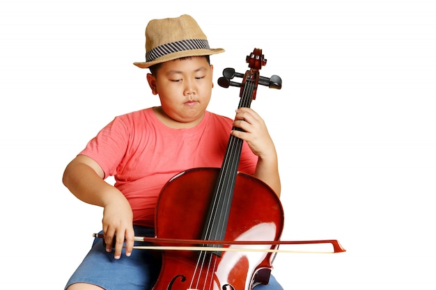 Un grasso ragazzo asiatico che indossa un cappello che indossa una camicia rosa che suona la musica per violoncello. isolato