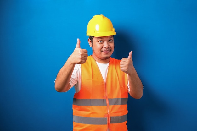 Fat asian construction worker wearing orange safety vest and helmet showing thumb up sign smiling