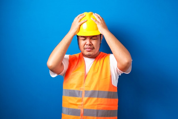 頭に手で強調された安全ヘルメットを身に着けている太ったアジアの建設労働者の男