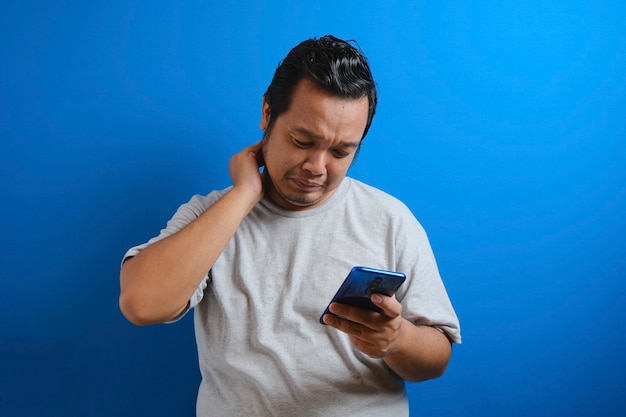 Fat Asian guy wearing a gray T-shirt looks sad reading online news from his cellphone. man shows disappointed gesture by wiping tears from his face