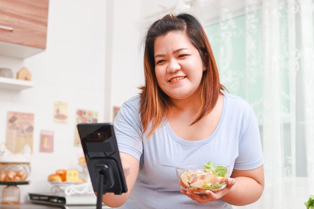 Una donna asiatica grassa cucina cibo biologico nella sua cucina di casa registra video online tramite smartphone pubblica contenuti sui social media concetto di influencer cucina sana per dimagrire