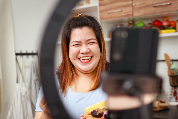 Fat Asian woman cooks organic food in her kitchen at home Record online video via smartphone Make content published on social media Influencer concept healthy cooking for weight loss