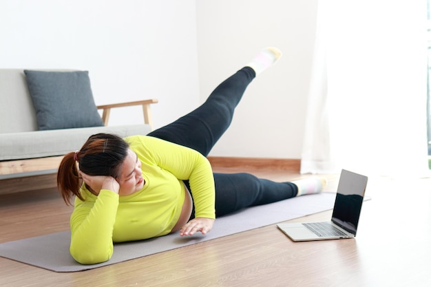 Foto le donne asiatiche grasse si esercitano per perdere peso sdraiate sul pavimento di legno in casa eseguono esercizi seguendo i formatori di fitness video online sul tuo computer portatile concetto di sport esercizio sano