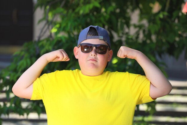 Fat boy in a yellow T-shirt and sunglasses shows muscles. High quality photo