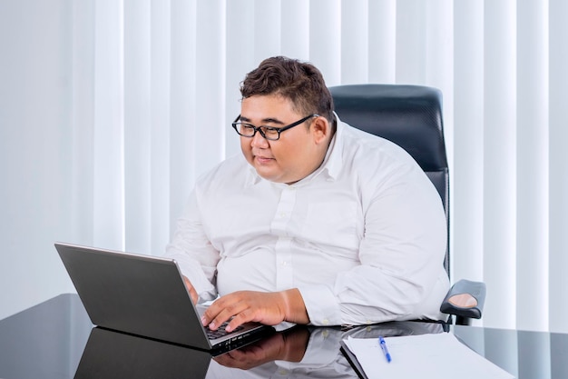 Fat businessman with glasses working at his laptop