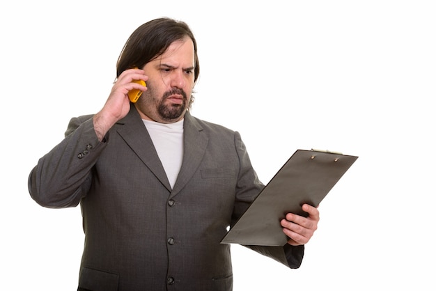 Fat Caucasian businessman looking confused while talking on phone and reading on clipboard