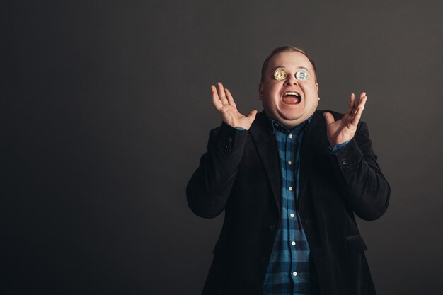 Fat celebrating man make crazy face.crazy bitcoin lover with golden coin on his eyes