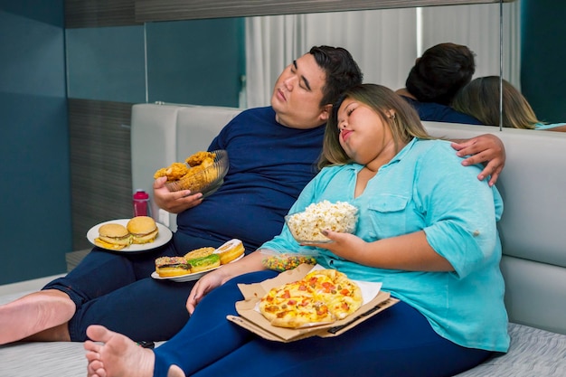 Photo fat couple sleeping while eating and watching