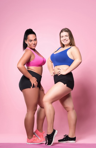 Fat but fit. Full length portrait of two youthful pretty overweight ladies standing with hands on hips.