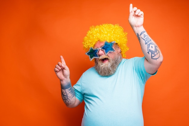 Fat happy man with beard tattoos and sunglasses dances music on a disco