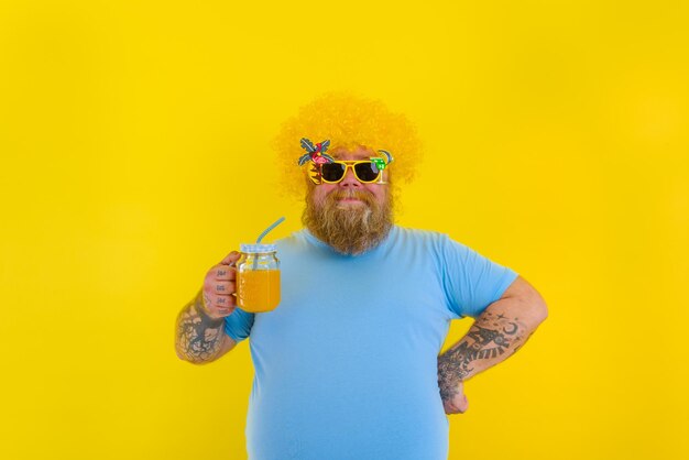 Fat happy man with wig in head and sunglasses drinks a fruit juice