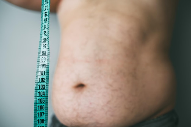 Foto l'uomo grasso controlla il suo grasso corporeo con un nastro di misurazione per lo sfondo bianco o obesità
