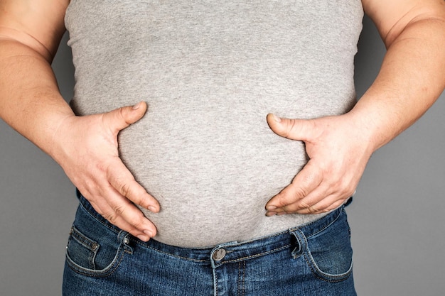 Fat man checking his weight on a gray background