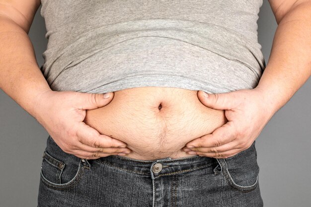 Photo fat man checking his weight on a gray background