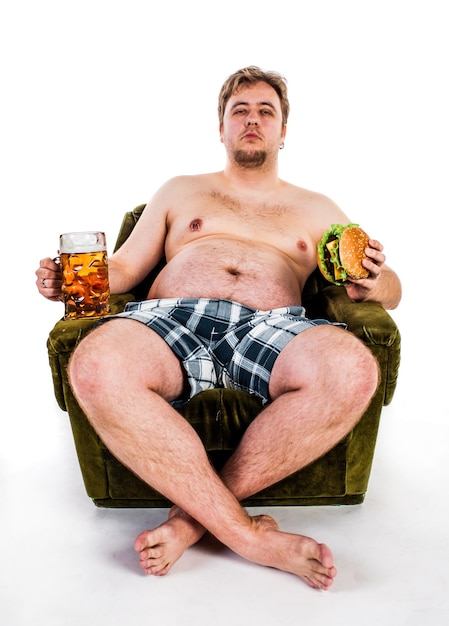 Photo fat man eating hamburger seated on armchair