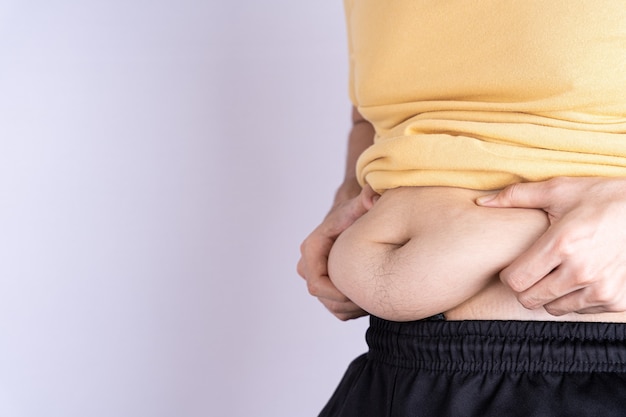 Photo fat man holding excessive fat belly isolated grey background.