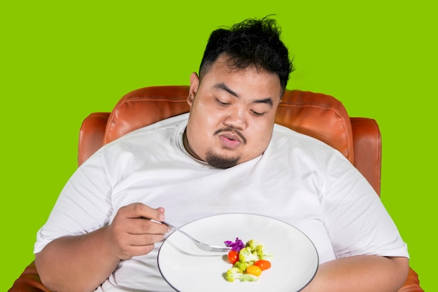 Fat man looks bored to eat healthy food on studio