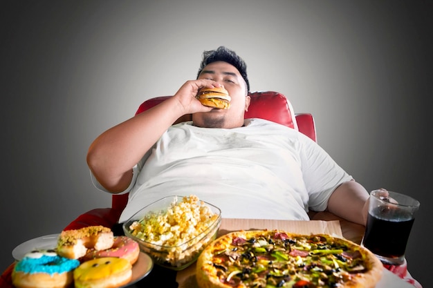 Fat man looks greedy with junk foods on the sofa