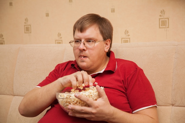 Fat man watching TV eating popcorn