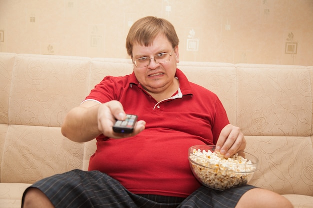 Fat man watching TV eating popcorn