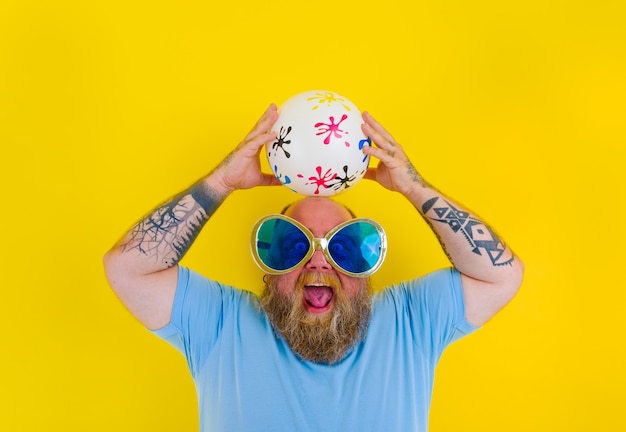 Fat man with beard and sunglasses have fun with a ball