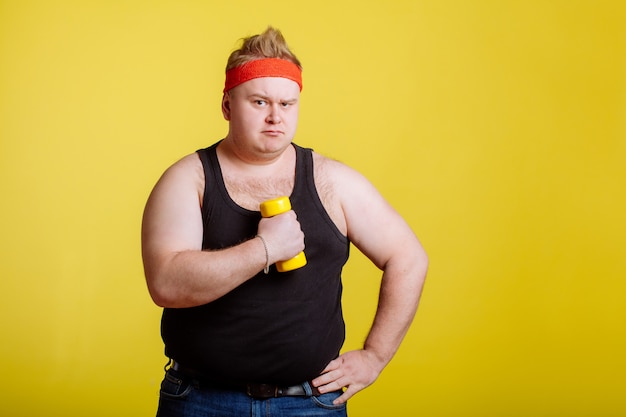 Fat man with dumbbell on yellow wall. Motivation for fat people