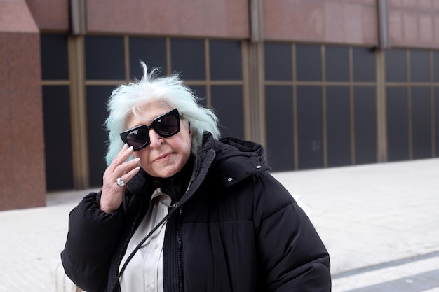 Fat older woman in coat and big black sunglasses looking at camera outdoors