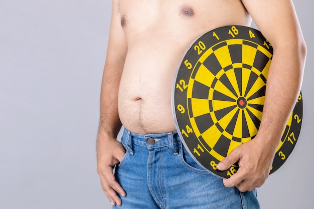 Fat people holding round yellow dartboard beside his belly position. Target of losing weight concept.