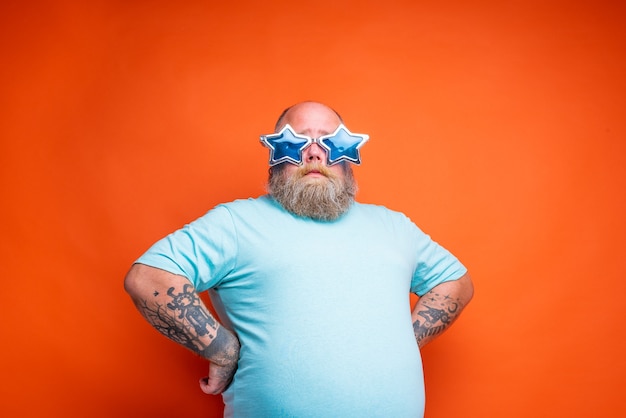 Photo fat thoughtful man with beard tattoos and sunglasses is unsure for something