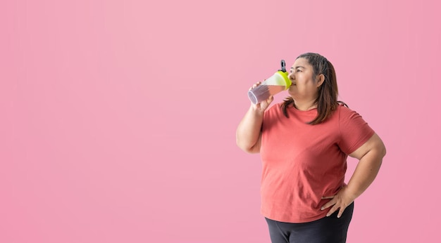 ピンクの背景に分離された水やサプリメントのボトルを飲む太った女性