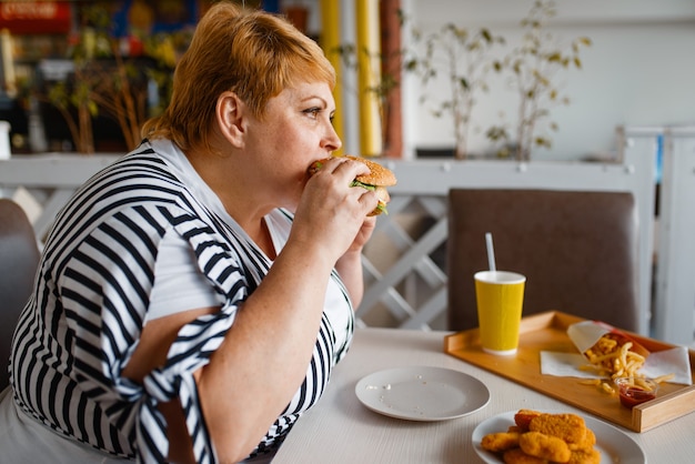 Fat Woman Eating Burger In Mall Food Court.