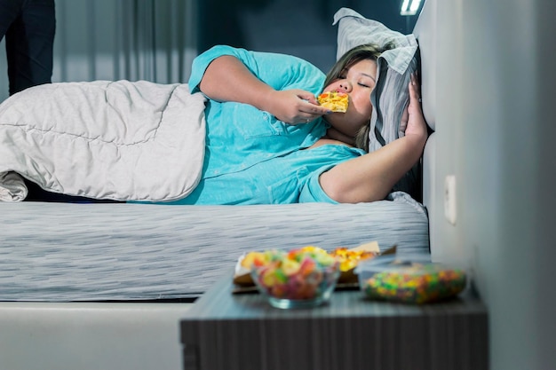 Fat woman eating pizza while lying on her bed