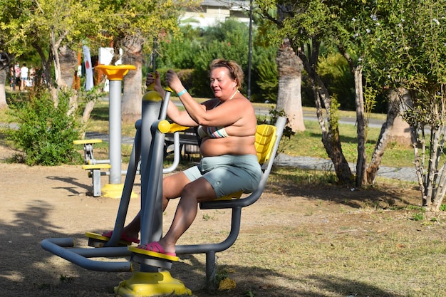 Fat woman goes in for sports on the street simulator. fat lady doing physical exercises on the sports ground