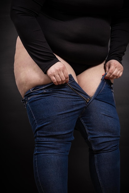 Fat woman pulling jeans on her legs on a black background